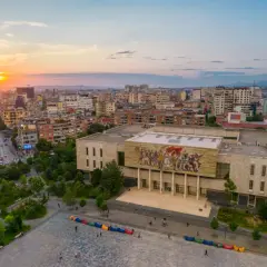 Zachód słońca nad Tiraną, ukazujący plac Skanderbega z monumentalnym budynkiem i mozaiką. To jedna z głównych tirana atrakcje.