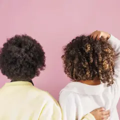 Dos personas con cabello rizado, una con afro oscuro y otra con rizos castaños, muestran la belleza natural de su cabello, quizás inspiradas por el método no poo.