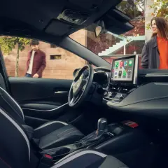 Wnętrze nowoczesnej corolla sedan z ekranem multimedialnym. Na zewnątrz para ludzi.