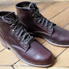 Bottes en cuir brun foncé, parfaites pour reconnaître le cuir gras. Le bois du parquet reflète la lumière sur le cuir.