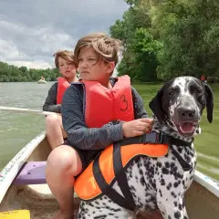 Dos niños y un dálmata disfrutan de un paseo en canoa, demostrando los beneficios de tener un perro en aventuras familiares.