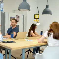 Junge Leute im **Master berufsbegleitend NRW** diskutieren an einem Tisch. Eine Frau schreibt an einer Tafel.