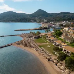 Piękna plaża z rzędami leżaków i parasoli, domki z dachówką, góry w tle. Idealne miejsce na wakacje, jak sugerują messonghi beach holiday resort opinie.