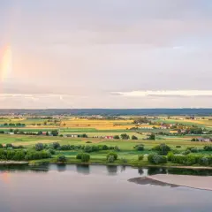 Krajobraz Kociewia nad rzeką, pola uprawne, domy i tęcza na niebie.