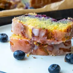 Zwei Scheiben saftiger zitronen blaubeer kuchen mit Zuckerguss und frischen Blaubeeren auf einem Teller.