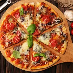 Pyszna pizza z pomidorkami i bazylią, obficie posypana serem do pizzy. Obok czosnek, pomidorki i sos.