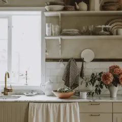 Köksbänk med diskho, kran och blommor. Skåpluckor i ljusbeige färg, redo att måla luckor för en ny stil.