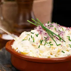 En krämig potatissallad toppad med rödlök och gräslök. Den ser ut att vara den godaste potatissalladen någonsin!