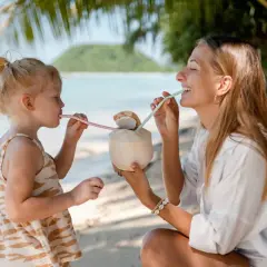 Mama i córka piją kokosa na plaży w Sanur. Słoneczny dzień, palmy i ocean tworzą rajski widok.