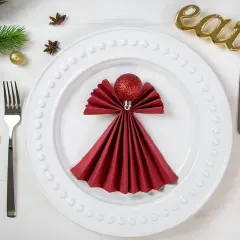Festlich gedeckter Tisch: Rote Servietten falten als Engel, daneben Gabel, Messer, Zimt, Sternanis und "eat"-Deko.
