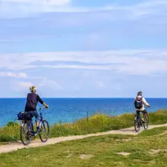 Dwie osoby na rowerach jadą ścieżką wzdłuż morza. To piękny dzień na przejażdżkę szlakiem rowerowym R10 na Mierzei Wiślanej.