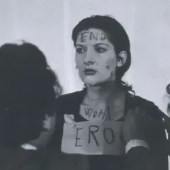Marina Abramović w performansie "Rhythm 0" z napisem "END" na czole i "WOMAN ERO" na klatce piersiowej.