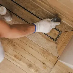 Mit Handschuhen und einem Werkzeug werden die Fugen auf dem Holzboden präzise gezogen.