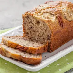 Pyszny chlebek bananowy fit z orzechami pekan i plasterkami banana na wierzchu, pokrojony na talerzu.