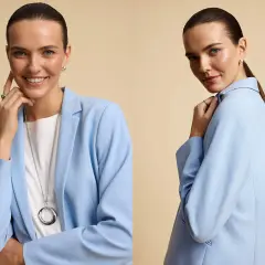 Kobieta w błękitnej marynarce i białej koszulce prezentuje stylowy total look. Długi naszyjnik i subtelna biżuteria dopełniają całość.