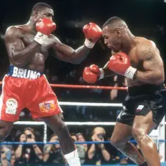 Two boxers, one in red shorts with "BRUNO" on the waistband, the other in black shorts, face off in a tense boxing match. The pressure fighter in red throws a punch.