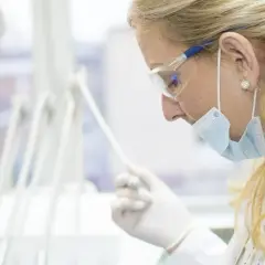 Dentystka w masce i okularach ochronnych trzyma narzędzie stomatologiczne.