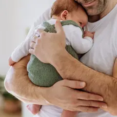 Ciepłe objęcia taty otulają maleńkie dziecko. Delikatne dłonie obejmują maluszka, tworząc bezpieczną przystań.