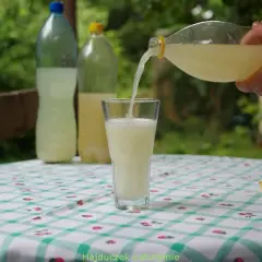 Domowy przepis na piwo imbirowe. Jasny napój nalewany z butelki do szklanki na tle zieleni.