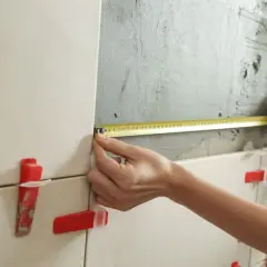 Precyzyjne układanie płytek 60x60 na ścianie. Miarka w dłoniach wyznacza kolejne etapy pracy.