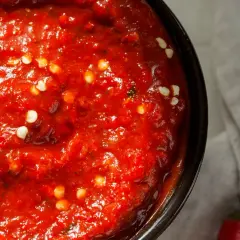 Nahaufnahme einer Schüssel mit leuchtend roter Harissa-Paste, gesprenkelt mit weißen Chiliflocken. Ein einfaches harissa rezept.