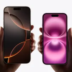 Dwie dłonie trzymają dwa iPhone'y. Jeden ma ciemny ekran z pomarańczowymi akcentami, drugi różowy. Oba modele mają dynamiczną wyspę.