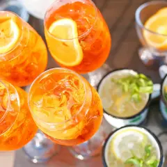 Orzeźwiający drink z prosecco, udekorowany plasterkiem pomarańczy, czeka na spróbowanie. Obok inne napoje z cytryną i miętą.