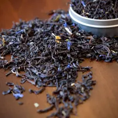 Garść liści aromatycznej herbaty earl grey, z niebieskimi płatkami chabru, rozsypana na drewnianym blacie.