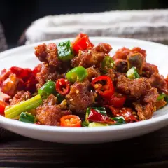 Chrupiący kurczak po kantońsku z papryczkami chili i zieloną cebulką na białym talerzu.