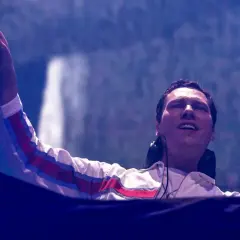 DJ Tiësto wznosi rękę, wskazując na tłum podczas jednego ze swoich energetycznych koncertów.