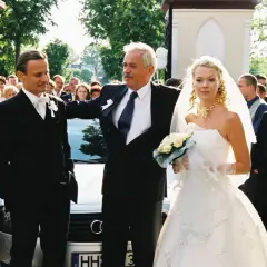 Wesele Wajda: pan młody, panna młoda i ojciec, otoczeni przez rodzinę i przyjaciół.