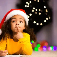 Ein kleines Mädchen mit Nikolausmütze denkt nach, während es am 6. Dezember ein Nikolausgedicht schreibt.