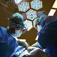Chirurdzy w sterylnych strojach pracują pod jasnym światłem lampy operacyjnej. Po zabiegu mogą wystąpić narkoza skutki uboczne.