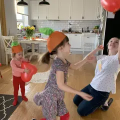 Dzieci w czapkach marchewek bawią się balonami w kuchni.