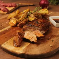 Pluma de porc recette : viande grillée juteuse, pommes de terre rôties et sauce savoureuse sur une planche en bois.