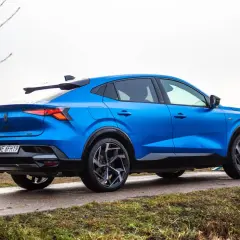 Niebieski Renault Rafale z dynamiczną linią dachu, zaparkowany na mokrej drodze.