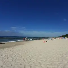 Słoneczna plaża wschodnia Ustka z ludźmi spacerującymi i odpoczywającymi na piasku.