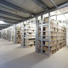Lagerhalle mit vielen Regalen voller Kartons. Ein Gabelstapler fährt durch den Gang. Hier kann man einen Termin avisieren.