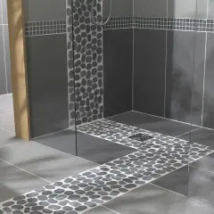Douche italienne moderne avec carrelage imitation pierre de galets sur le sol et les murs. Un banc en bois et des serviettes ajoutent une touche chaleureuse.