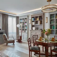 Eleganckie wnętrze w stylu klasycznym. Okrągły stół z krzesłami, regały z książkami, obraz i wygodny fotel tworzą przytulną atmosferę.