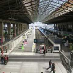 Intérieur lumineux de la gare du Nord, avec des quais, des voies ferrées et des trains. Des voyageurs circulent sous la grande verrière.