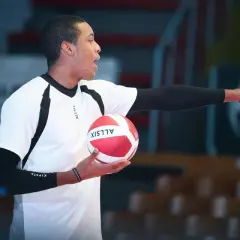 Mężczyzna w białej koszulce z czarnymi wstawkami trzyma czerwoną piłkę do siatkówki i wskazuje palcem. To jego ile challenge w siatkówce.