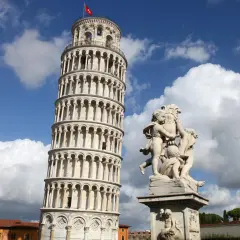 La Torre Pendente di Pisa, con la sua inconfondibile inclinazione, si erge maestosa sotto un cielo azzurro e nuvoloso, accanto a una scultura di putti.