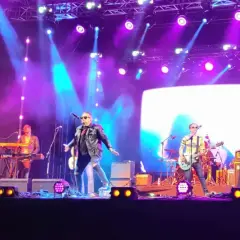 Zespół gra na scenie podczas koncertów w Stalowej Woli. Wokalista w skórzanej kurtce, gitarzyści i klawiszowiec.