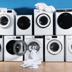 Mehrere weiße Waschmaschinen, einige mit Wäsche, stapeln sich vor blauem Hintergrund. Eine pflegeleicht waschmaschine mit offener Tür und herausfallendem Handtuch.