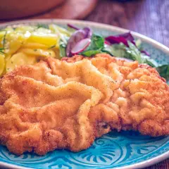 Ein knuspriges Schnitzel Wiener Art mit goldbrauner Panade, serviert mit Kartoffelsalat und frischem Grün.