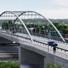 Nowoczesny most nad torami kolejowymi, po którym poruszają się samochody i rowerzyści. W tle widoczne kontenery i zieleń.