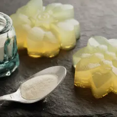 Proszek agar w słoiczku i na łyżce, obok galaretki w kształcie kwiatów. Agar to naturalny środek żelujący.