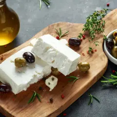 Kostki sera feta, oliwki, rozmaryn i oliwa z oliwek na drewnianej desce. Idealne składniki na grecką sałatkę.