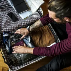 Mężczyzna pakuje walizkę: aparat, paszport, ubrania i mapę. Oto jak spakować walizkę na podróż.